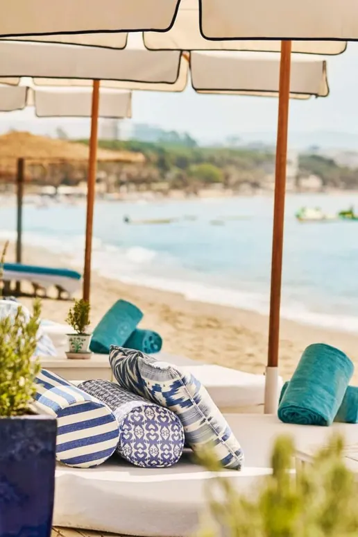Sun beds and striped cushions under parasols, the bay behind them