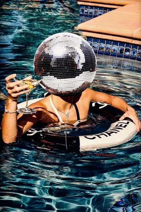 A swimmer in a pool wearing a mirrorball helmet, holding a martini